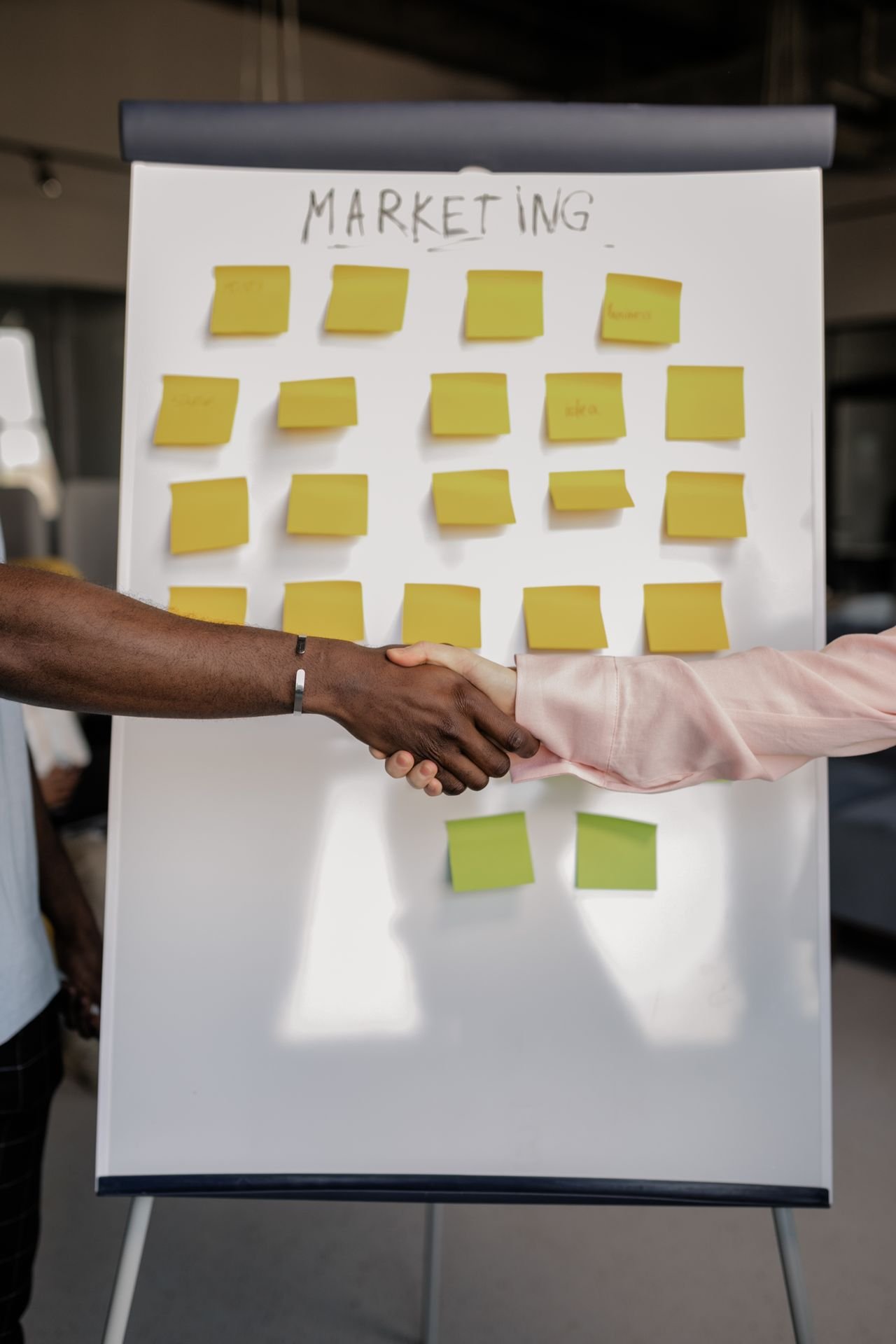 Two colleagues shaking hands in front of a marketing whiteboard