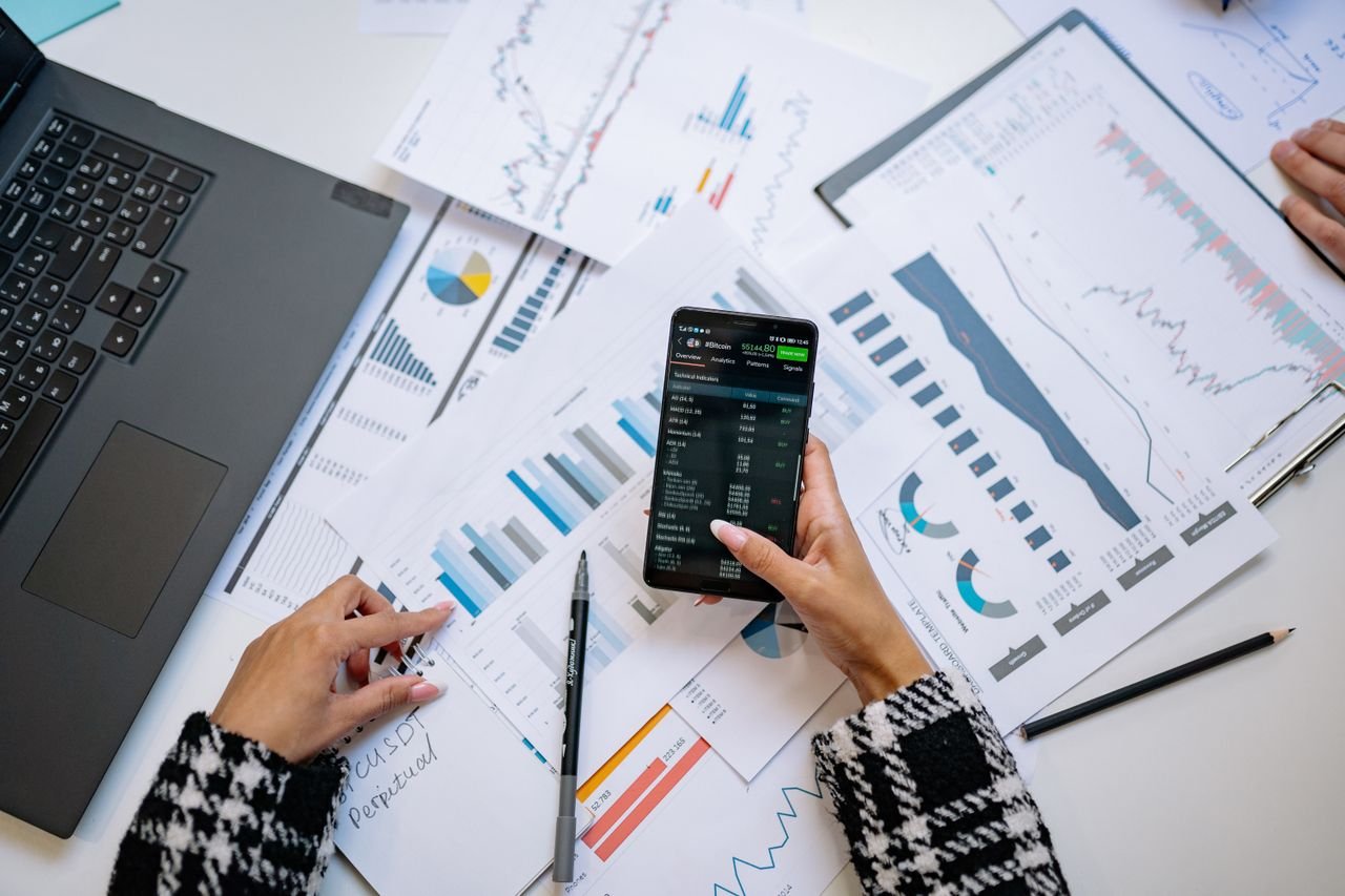 Hands reviewing performance analytics on a phone over printed charts